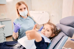 Dental staff member and child in a dental chair giving a thumbs up